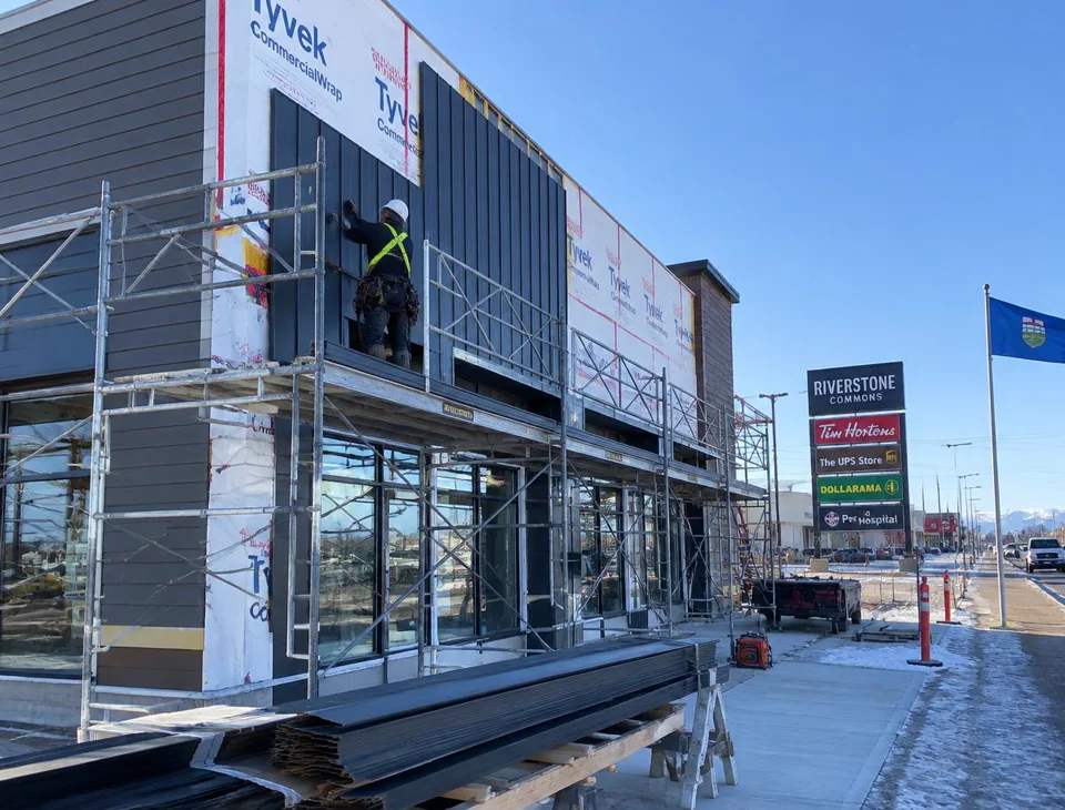 Commercial building exterior facade work with new siding panels installed from scaffolding